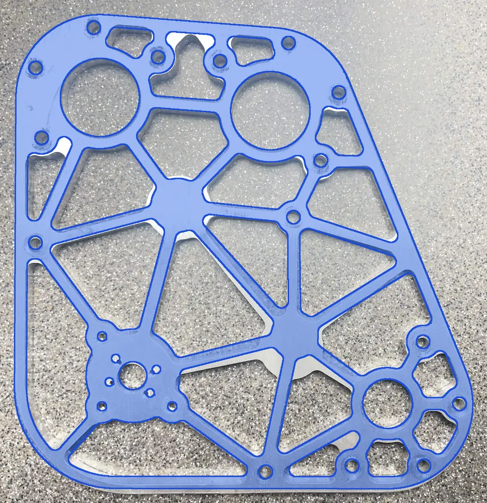 The reverse-engineered CAD model in blue laid over a photo of the original machined plate, lined up on the hole centers, with small slivers of bare aluminum where the two differ